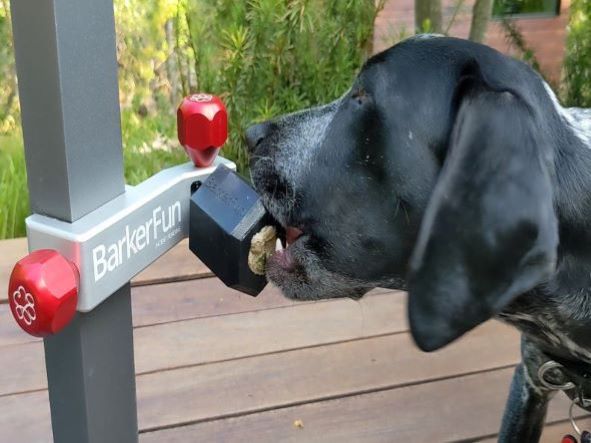 A Treat Clincher in silver with red handles attached to an outdoor table leg. A Zilla food container with frozen dog food is attached to the Treat Clincher.